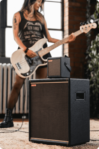 A bassist playing next to a Spark 2 stacked on a Spark CAB 2 in a sunlit room