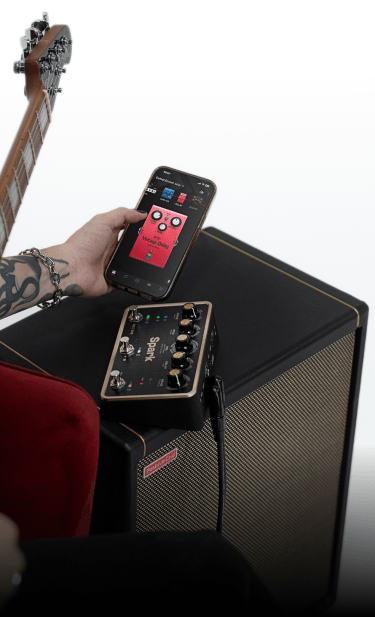 Guitarist tapping a tone on the Spark app, with Spark PEDAL and amp in the background